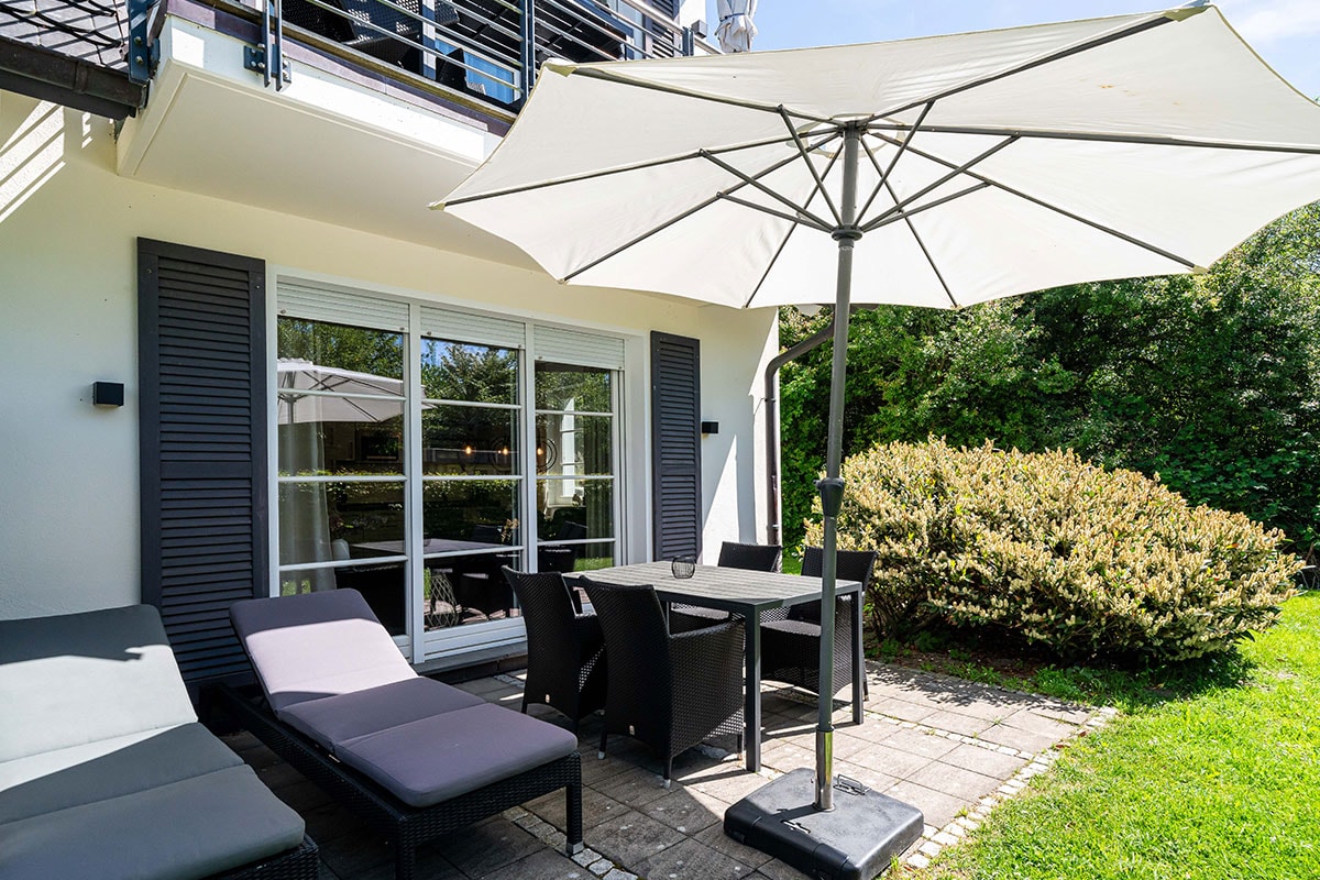 Terrace with dining table, chairs, parasol and two sun loungers in front of the Seeschwalbe vacation apartment in the Künstlerquartier Seezeichen.