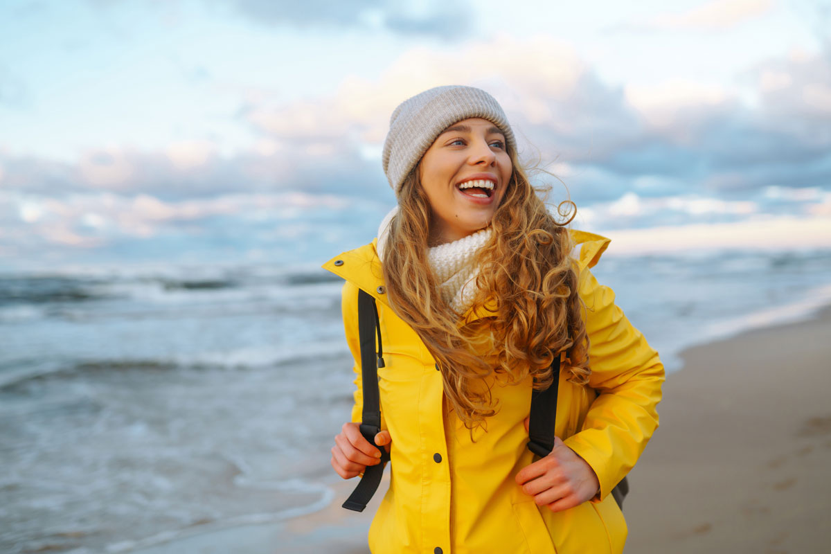 Glückliche Frau in Regenbekleidung am Ostseestrand bei einem Herbstangebot im Vju Hotel auf Rügen.