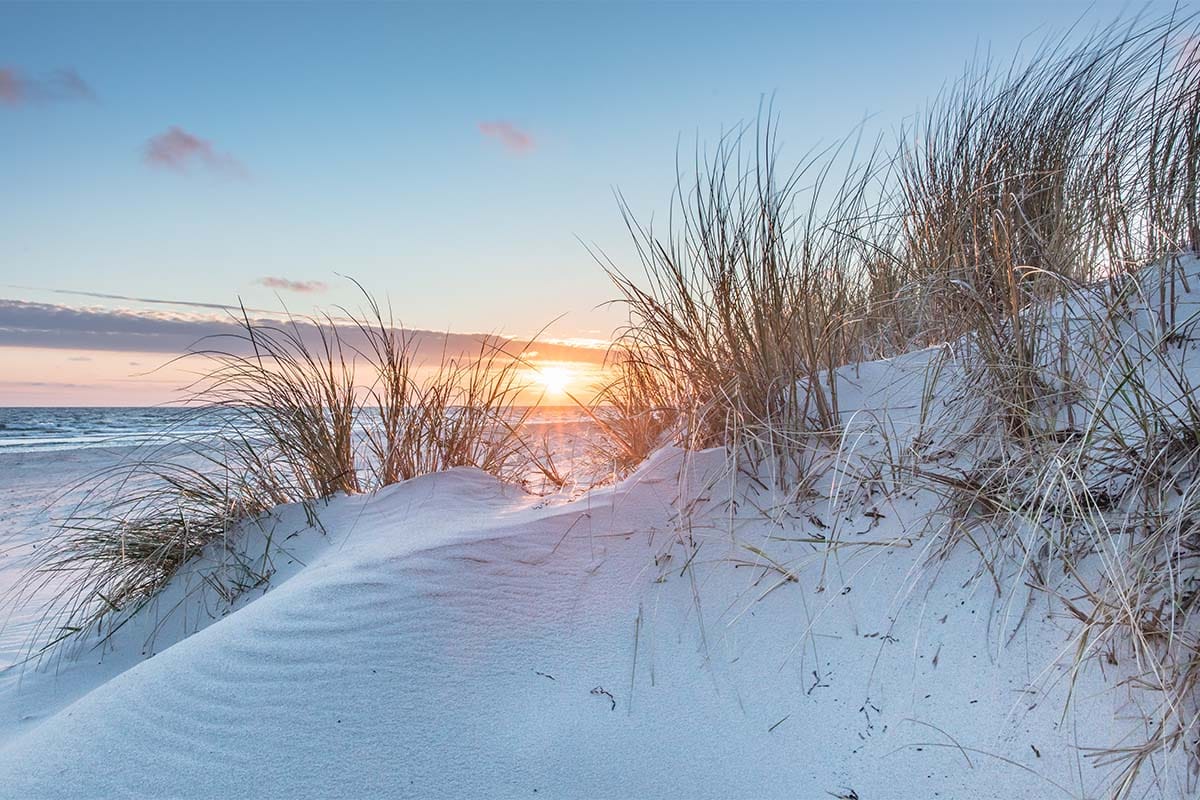 Eine verschneite Düne mit Blick auf das Meer und Sonne am winterlichen Ostseehimmel.