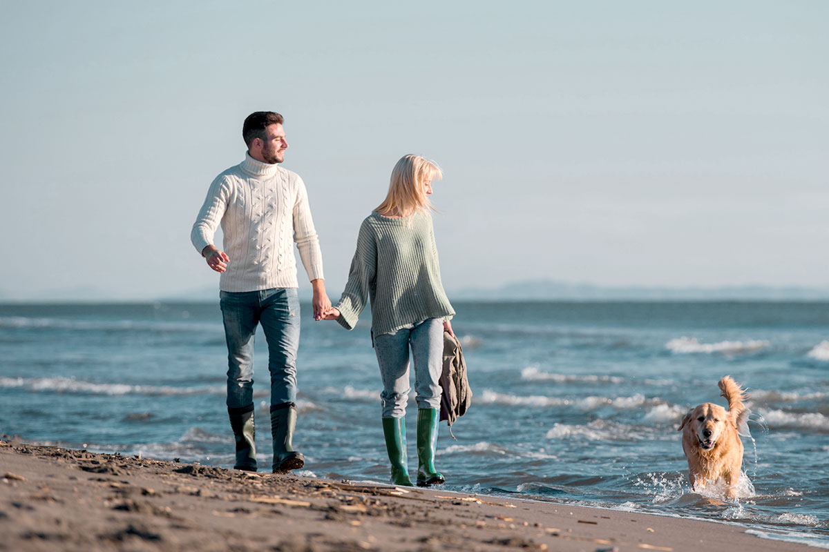 Pärchen beim Wandern am Strand mit Hund bei einem der zahlreichen Urlaubsangebote vom Vju Hotel.