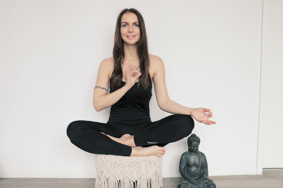 Kati Blödorn in schwarzer Kleidung sitzt im Vju Hotel in Meditationshaltung mit Buddha-Statue im Hintergrund.
