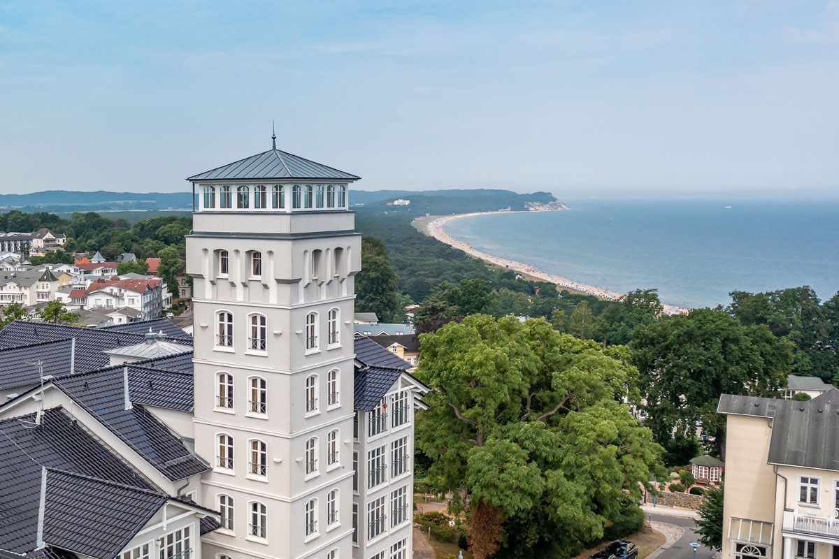 Außenansicht des Vju Hotels mit markantem Turm, weißen Fassaden und Blick auf die Küste von Rügen.