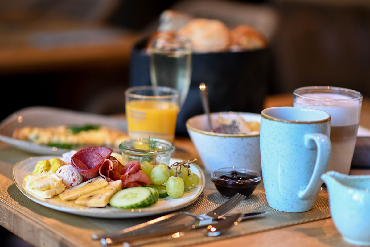 Ein gedeckter Frühstückstisch mit Kaffee, Saft, frischem Obst, Aufschnitt, Käse und Brötchen im Vju Hotel auf Rügen.