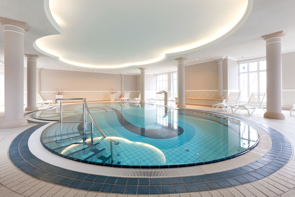Ein stilvoller Innenpool mit geschwungenen Formen und edlen Säulen im Wellnessbereichs des Vju Hotel auf Rügen.