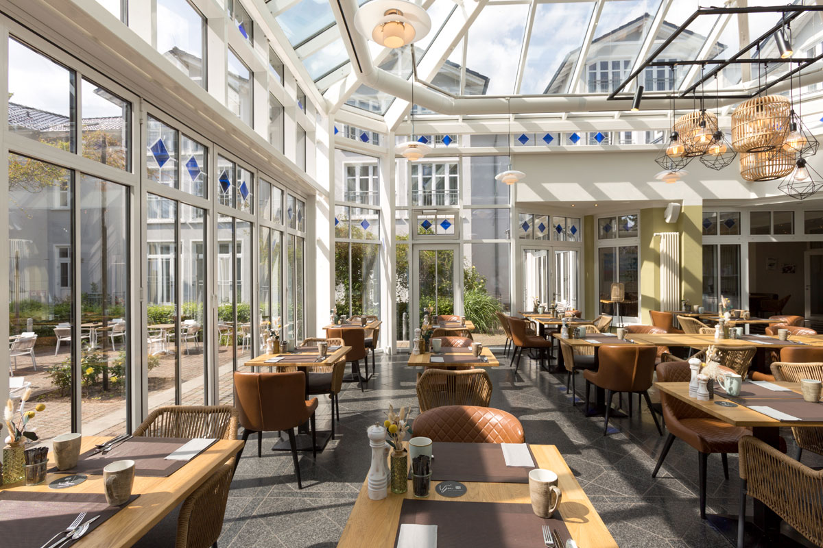 Ein großzügiger Wintergarten mit Glasdach, stilvollen Möbeln und viel Tageslicht im Vju Hotel auf Rügen.