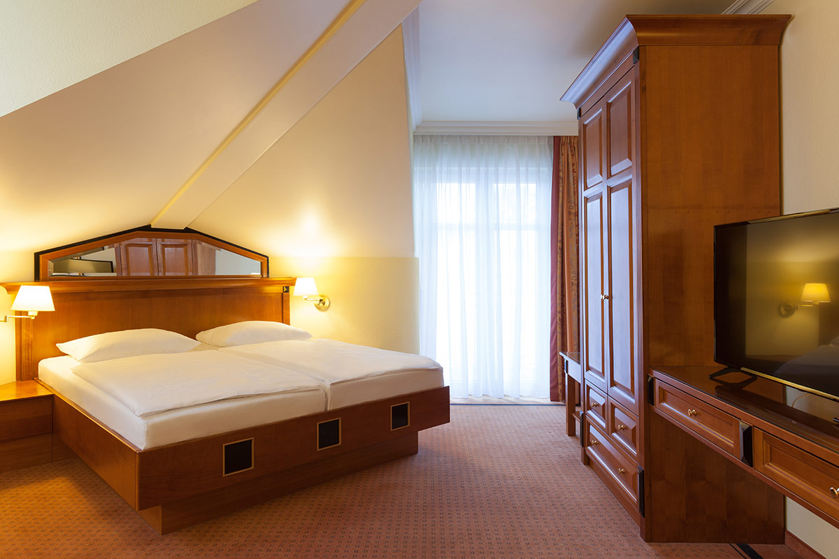 Gemütliches Hotelzimmer in den Dependancen im Vju Hotel mit warmen Holzmöbeln, großem Doppelbett und Balkonzugang.