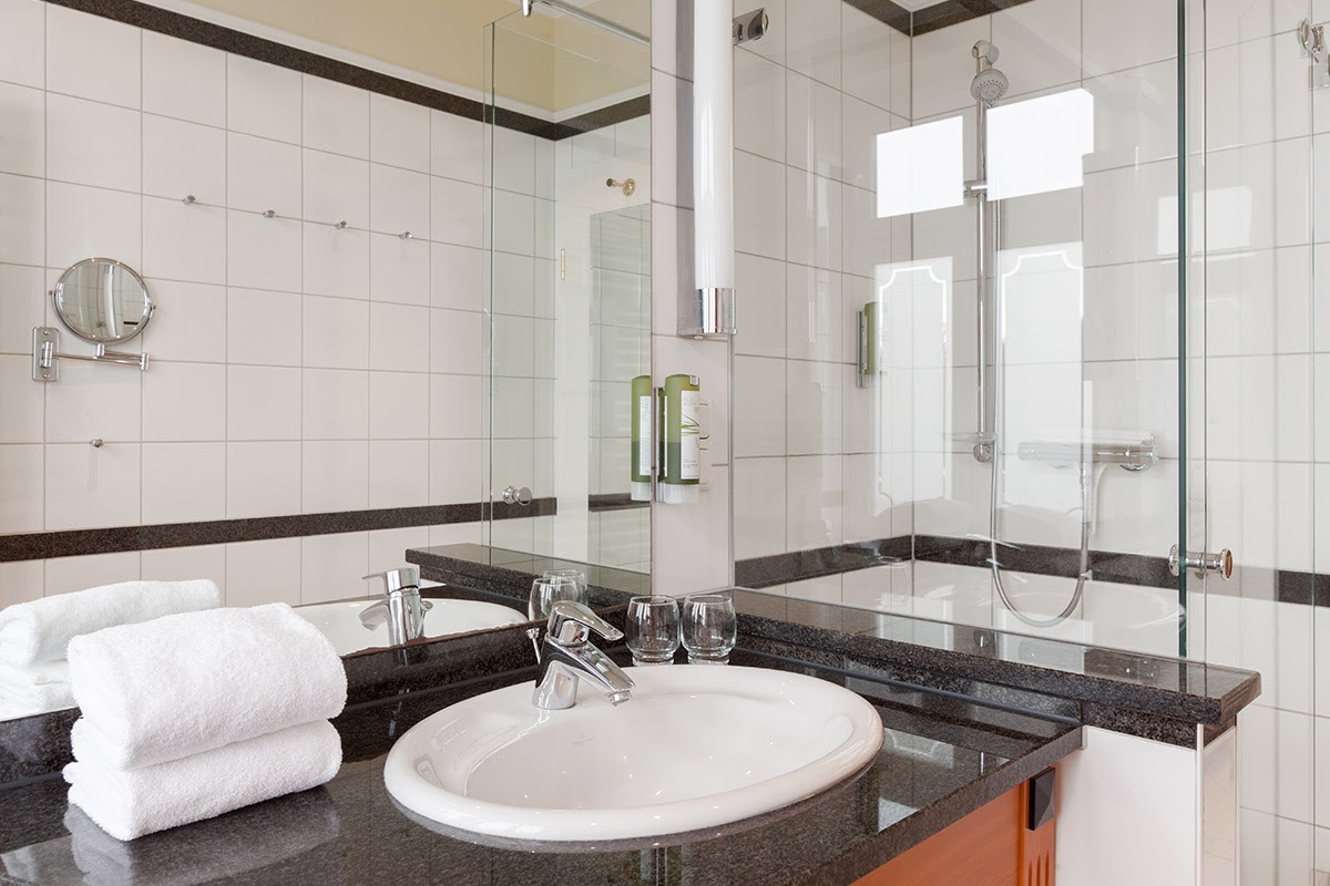 Modern bathroom with glass shower, washbasin, mirror and towels in the double room of the Vju Hotel annexes.