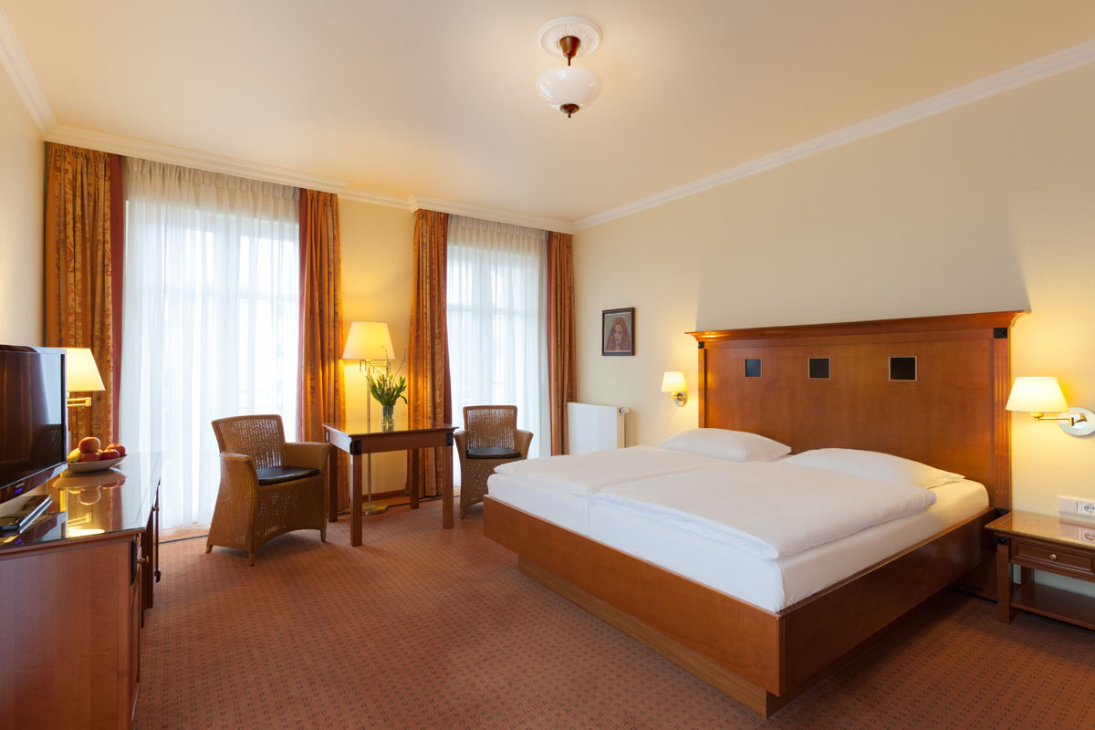 Großzügiges Doppelzimmer mit stilvollen Holzmöbeln, großem Bett und Sitzbereich im Doppelzimmer der Dependancen im Vju Hotel.