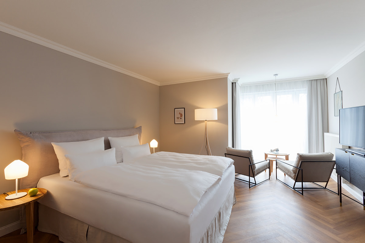 Bright double room with comfortable bed, reading corner and desk at the Vju Hotel on Rügen.