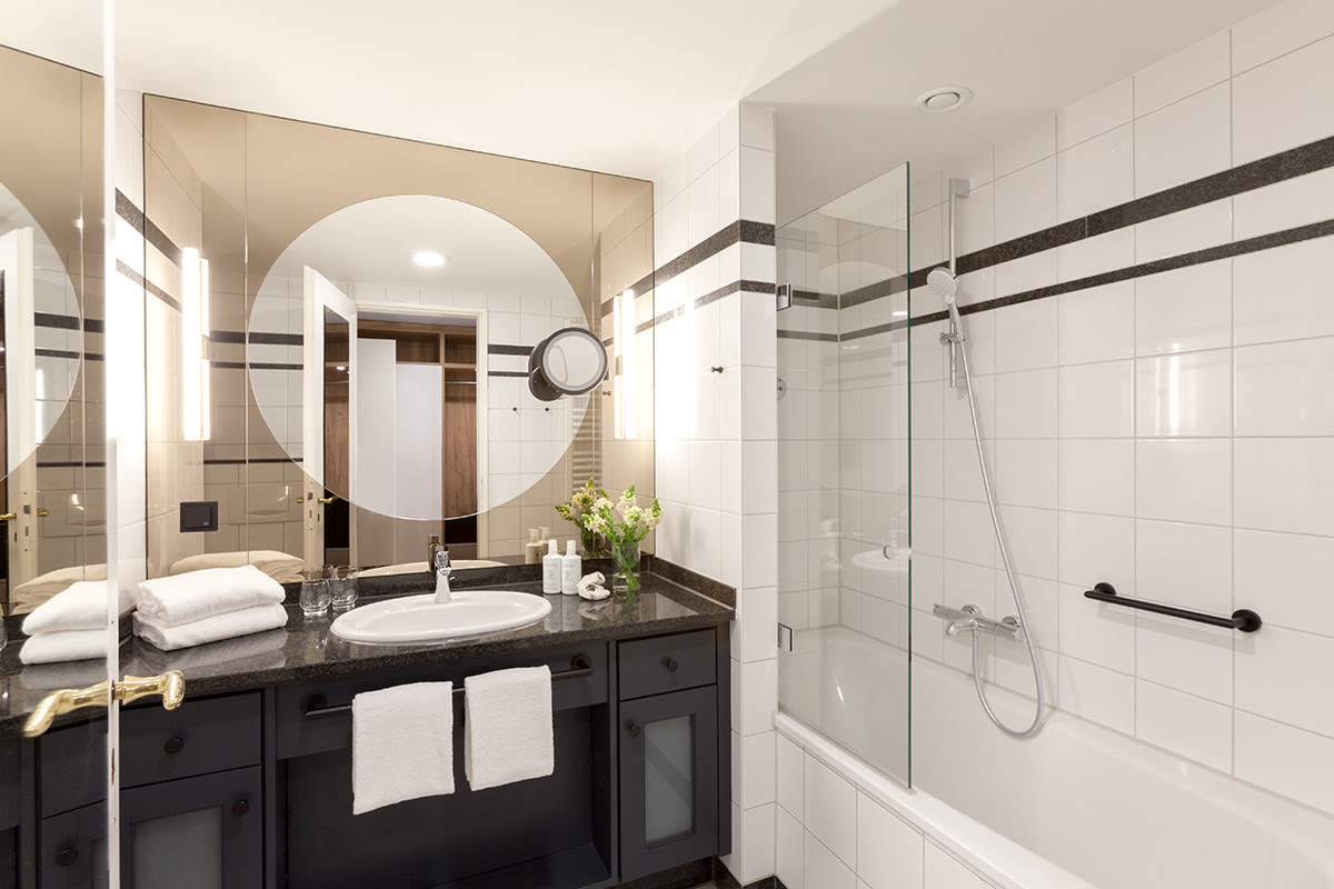 Bright bathroom with glass shower, large mirror wall and black accents in the double room of the Vju Hotel.