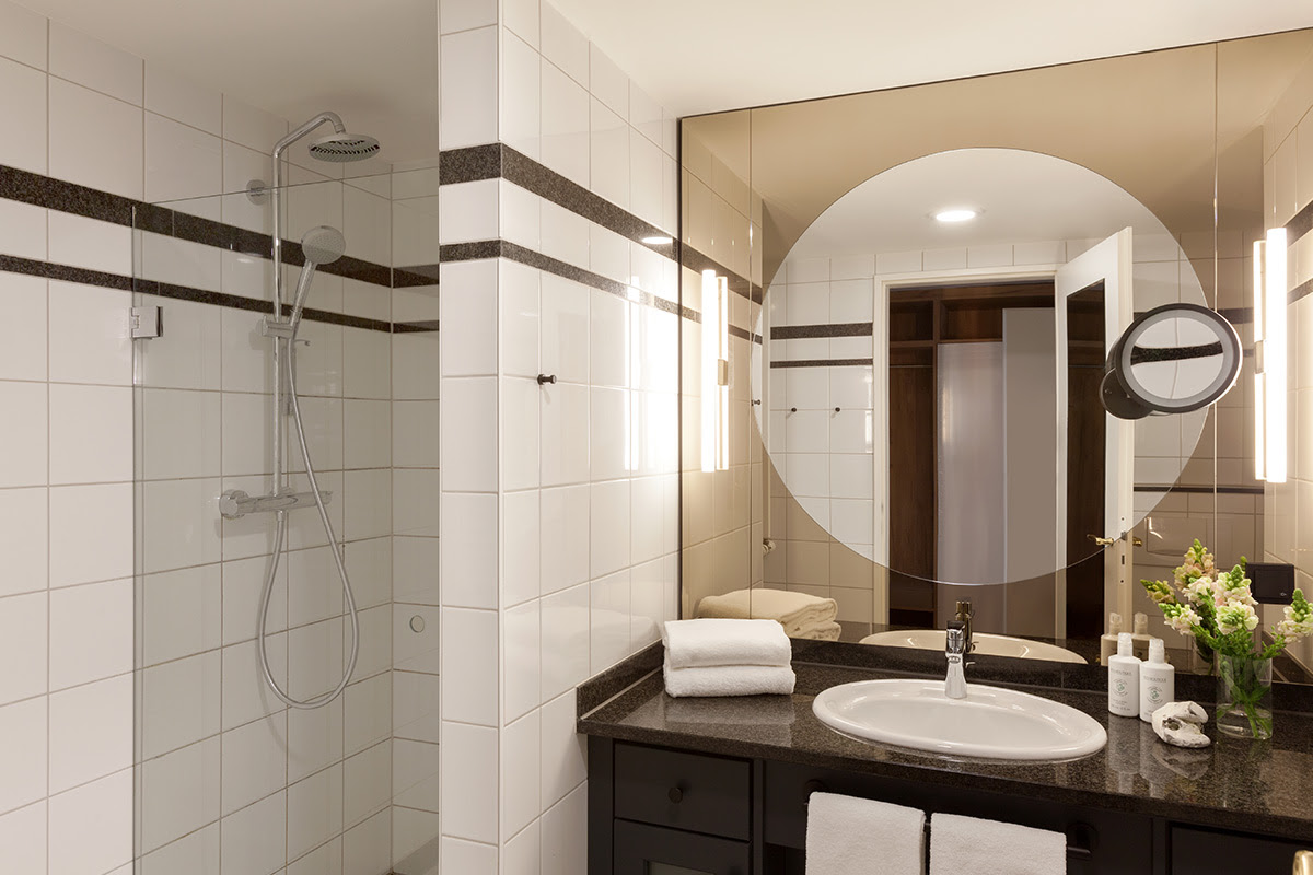 Stilvolles Hotelbad mit geräumiger Regendusche, Marmorwaschtisch und runden Spiegeln im Doppelzimmer des Vju Hotels.