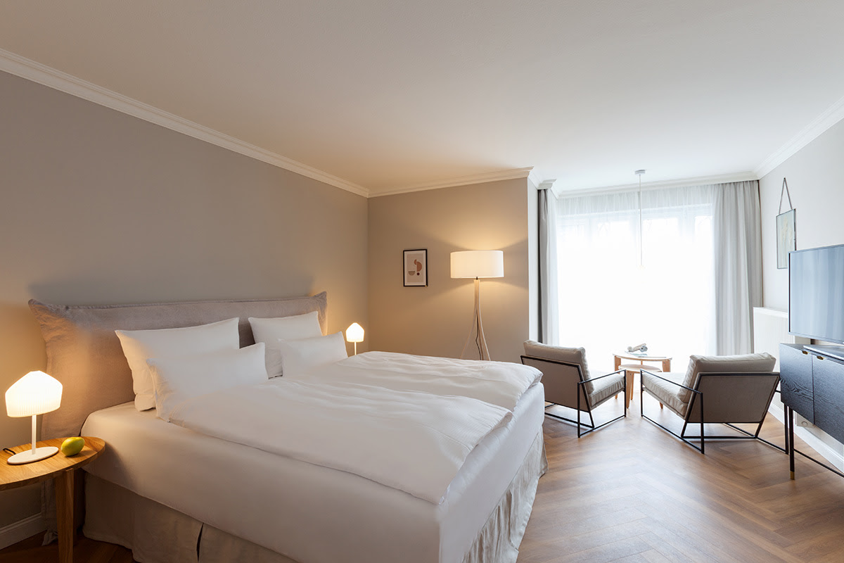 Modern eingerichtetes Doppelzimmer im Vju Hotel mit großem Bett, Sitzecke, TV, Holzfußboden und bodentiefem Fenster.