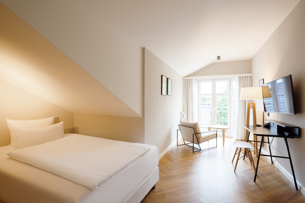 Einladendes Queensize-Einzelzimmer im Vju Hotel mit bequemer Sitzecke, Schreibtisch, Fernseher und bodentiefem Fenster.