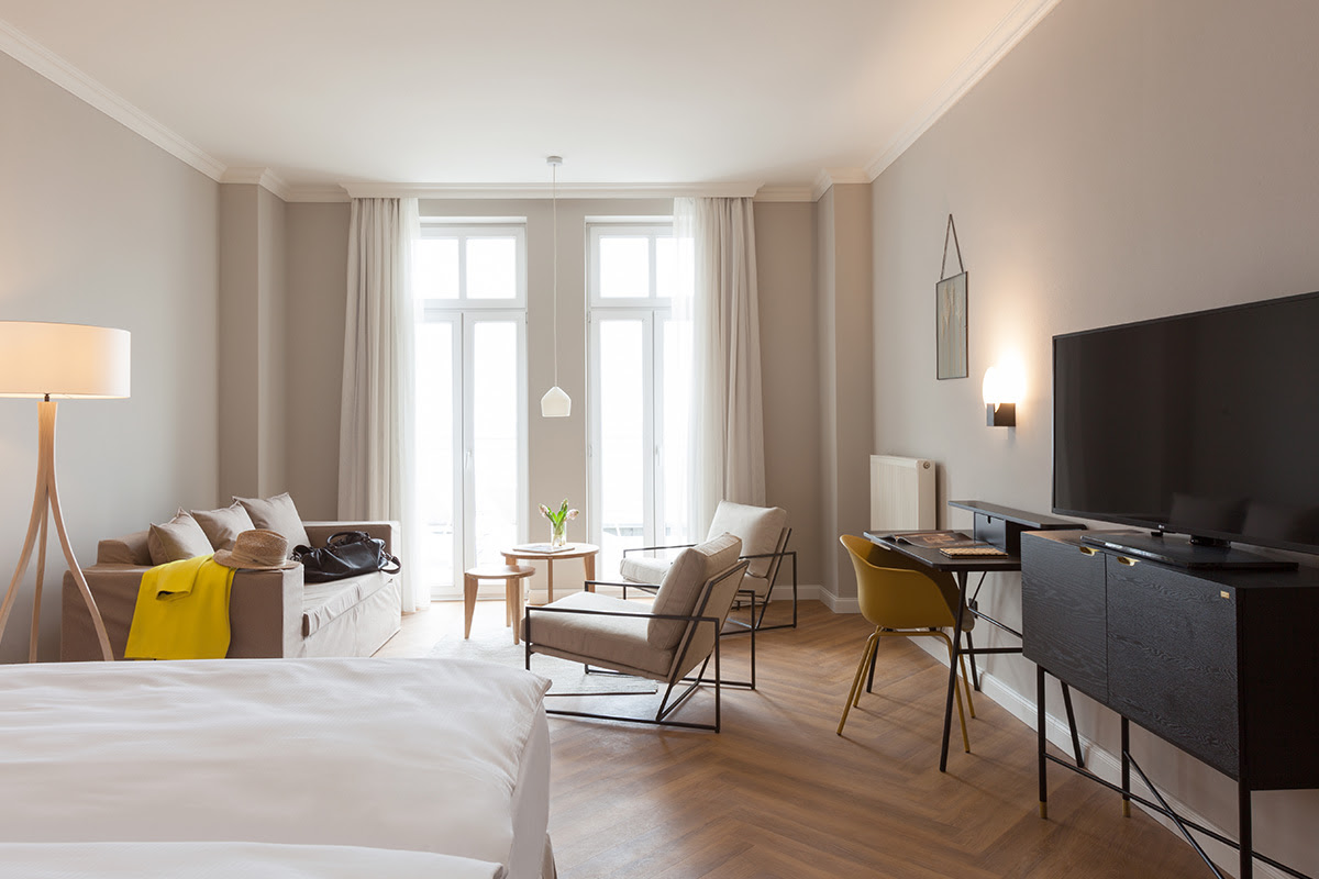 Modernes Studio im Vju Hotel mit großer Fensterfront, Sofa, Sesseln, Schreibtisch und Blick auf die Ostsee.