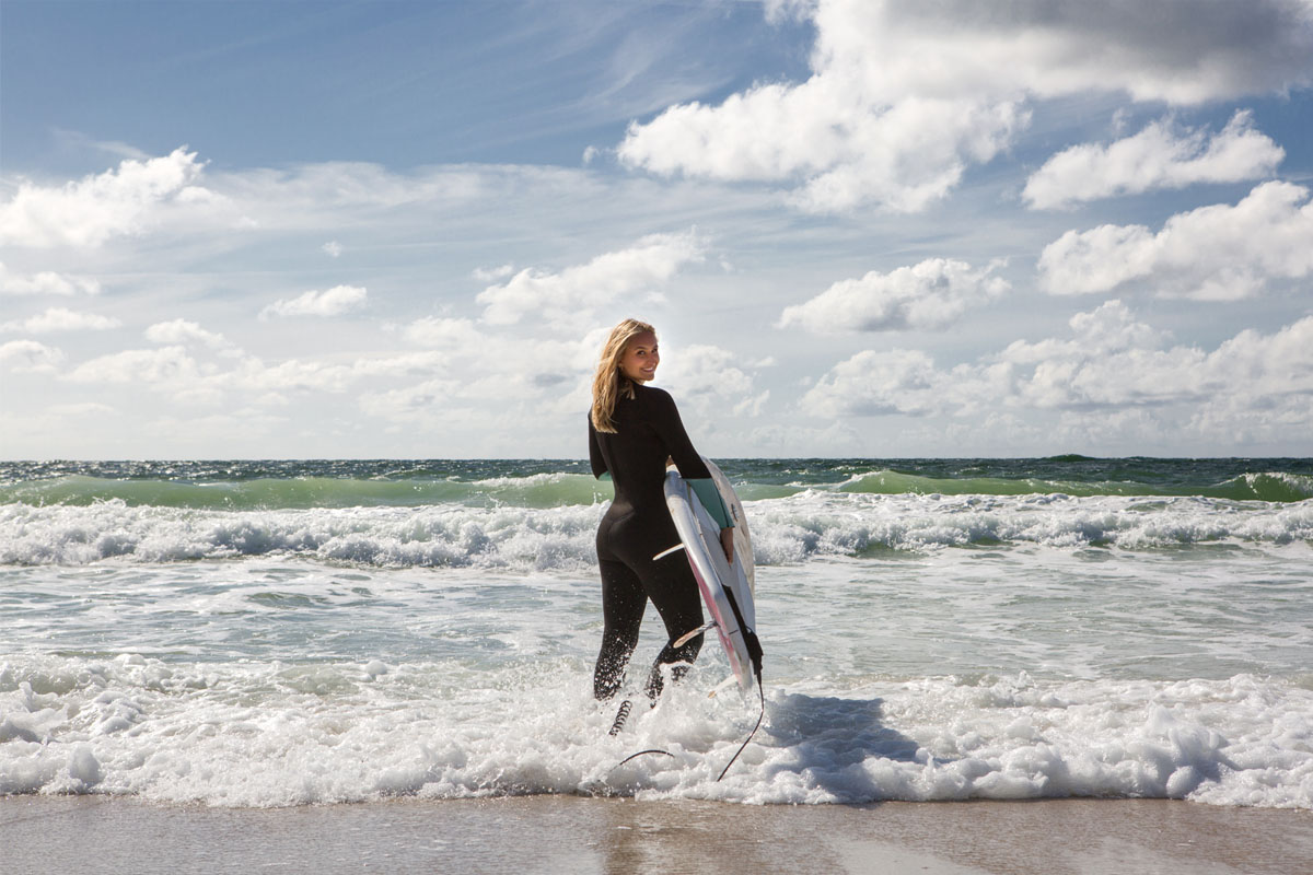 Surferin im Neoprenanzug mit Surfbrett in den Wellen stehend im Aktivurlaub im Wyn. Strandhotel auf Sylt.