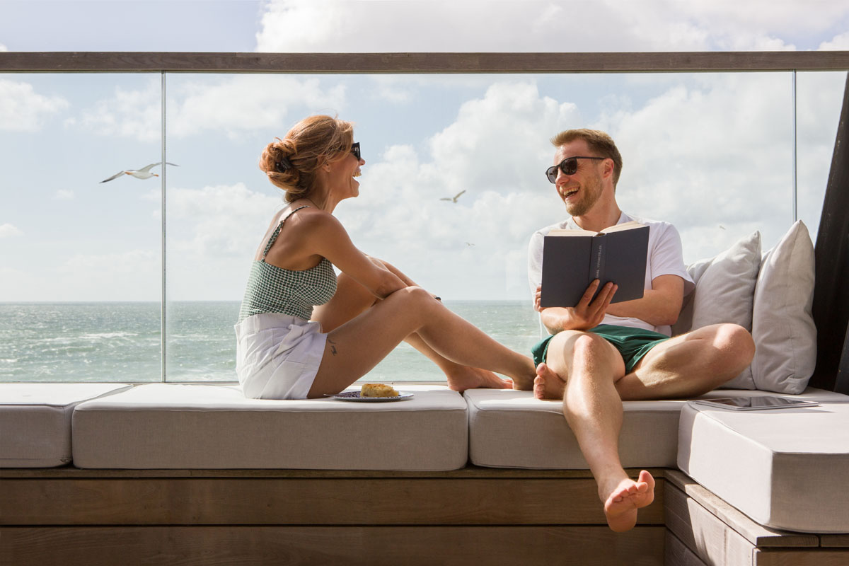 Ein Paar genießt entspannte Momente auf einer Terrasse mit Meerblick im Wyn. Strandhotel mit dem Angebot Wynsch Zweisamkeit.