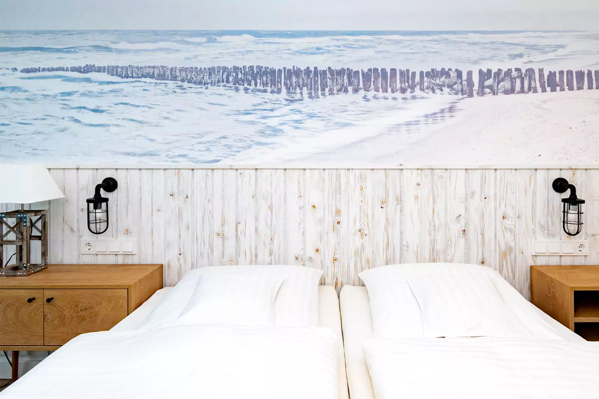 Zimmer mit Doppelbett, rustikalen Holzmöbeln und einem maritimen Wandbild im Wyn. Strandhotel Sylt mit vielen Angeboten.