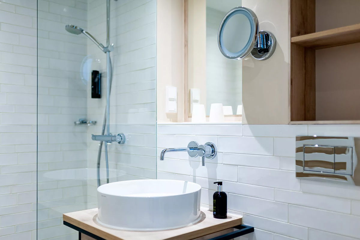 Helles Bad der Strandhafer Suite mit Regendusche, Waschtisch, Spiegel und modernen Akzenten im Wyn. Strandhotel.