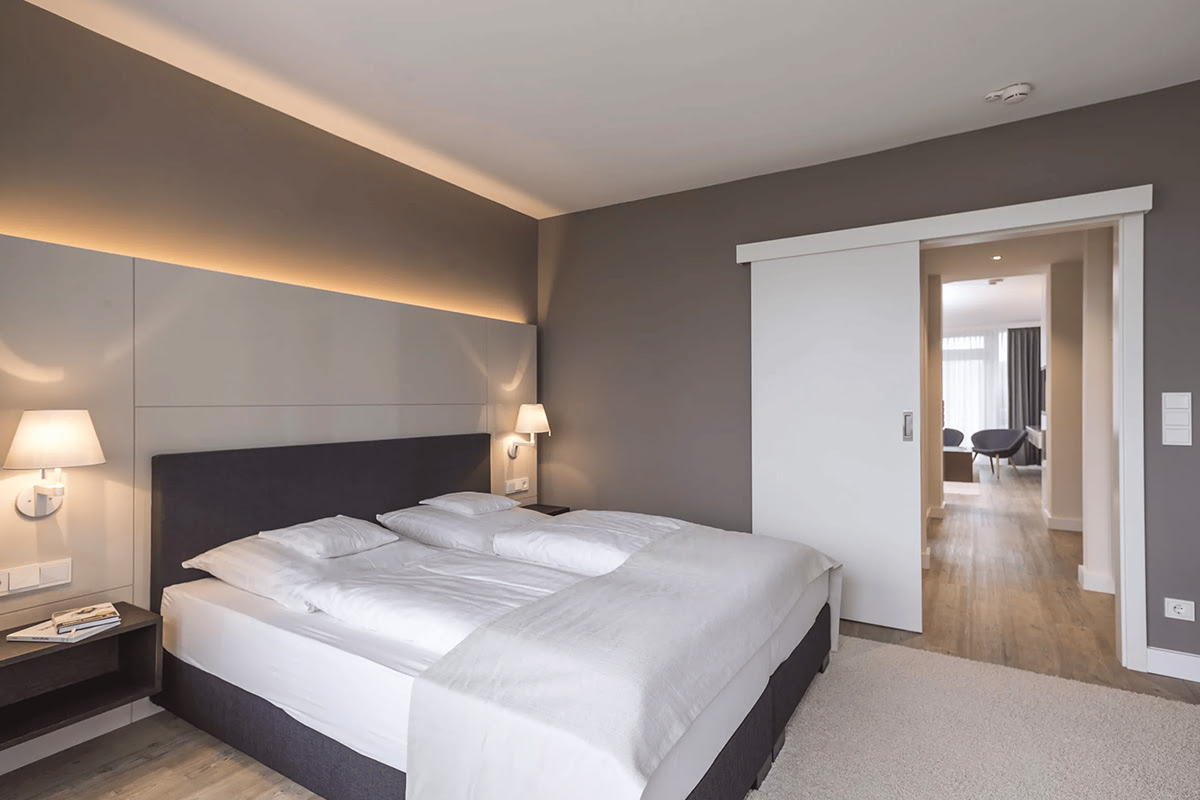 Großes Boxspringbett mit weißer Bettwäsche in der eleganten Strandlaeufer Suite des Wyn. Strandhotels.