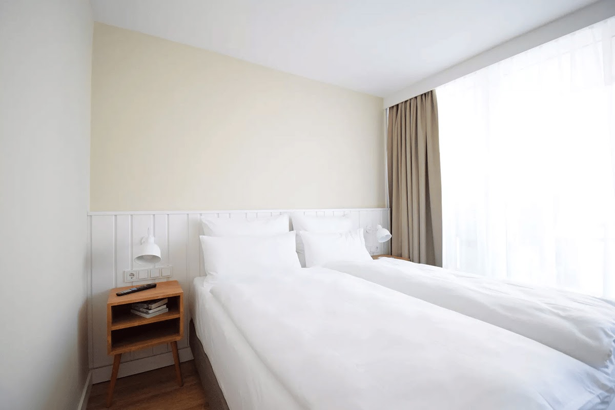 Minimalistisch eingerichtetes Zimmer "Land in Sicht" mit gemütlichem Bett und Vorhängen vor dem Fenster im Wyn. Strandhotel.