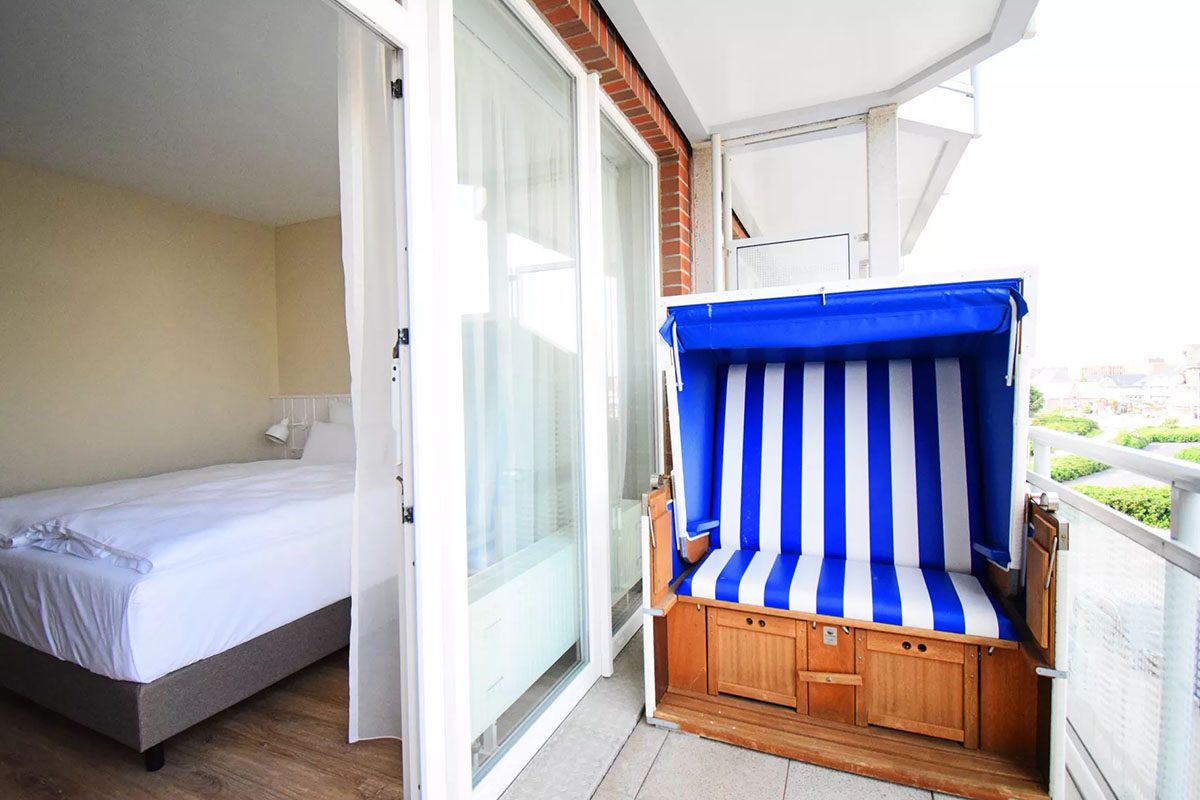Zimmer "Land in Sicht" im Wyn. Strandhotel mit Doppelbett und direktem Zugang zum Balkon mit blau-weißem Strandkorb.