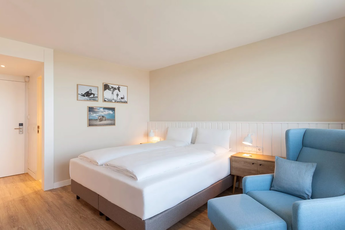 Einladendes Hotelzimmer Meerzeit mit komfortablem Bett, blauem Sessel und sanfter Beleuchtung im Wyn. Strandhotel.