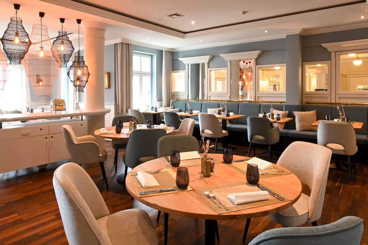 Blick in das maritime Restaurant Küstensilber mit hellen Stühlen und Bänlen, Holzdekor und eingedeckten Tischen im Vju Hotel auf Rügen.