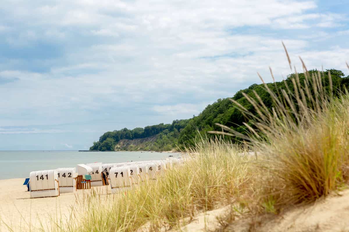 Ein ruhiger Ostseestrand auf Rügen mit Strandkörben, umgeben von Dünen und einer grünen Küstenlandschaft, die zum Entspannen einlädt.