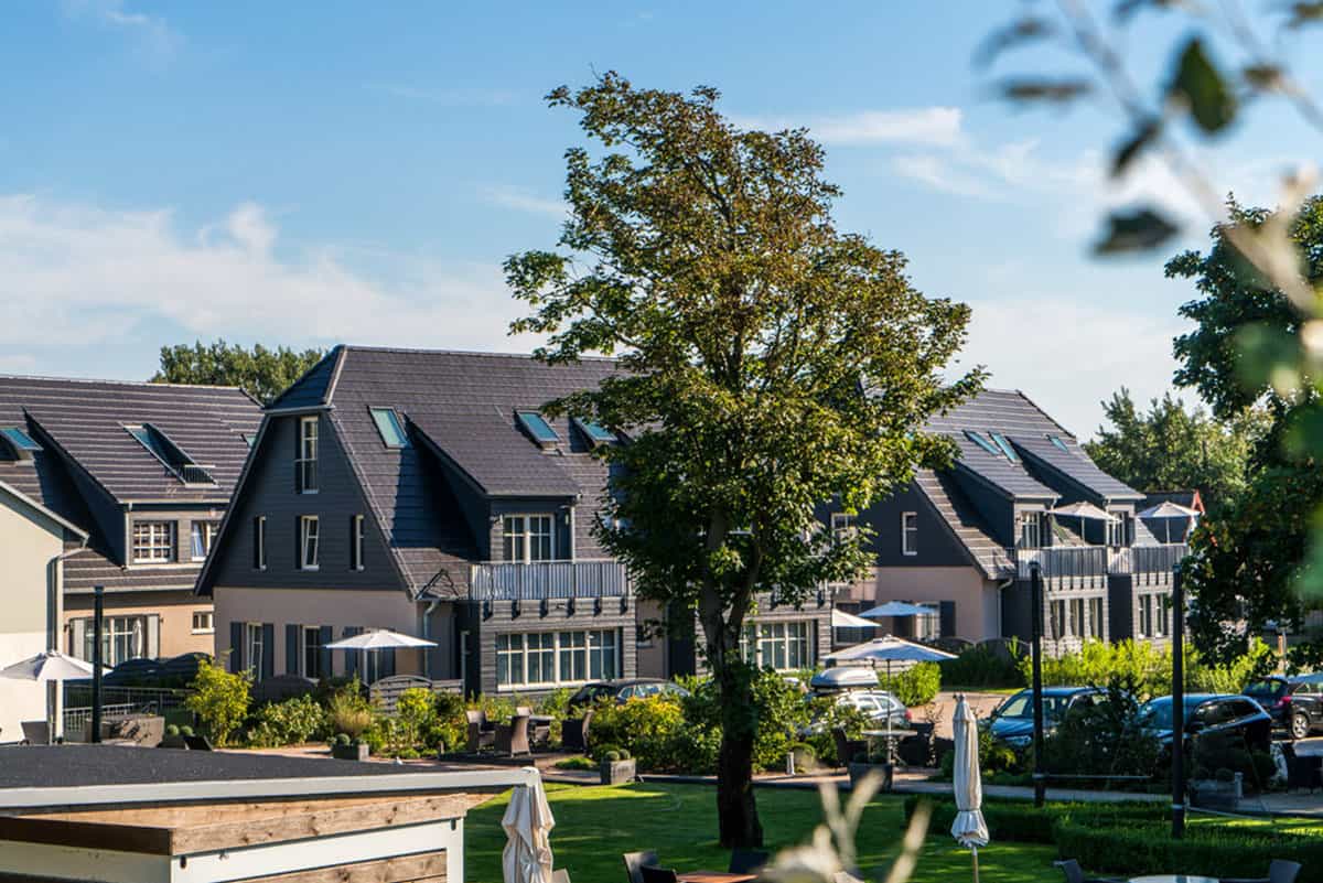 Moderne Ferienunterkünfte im Dünenpark Ahrenshoop Sonnenschirmen und Bäumen vor einer klaren, blauen Himmelkulisse.