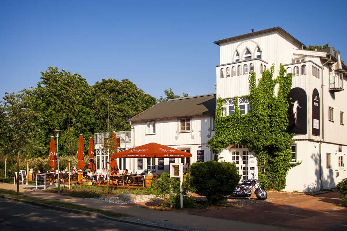 Außenansicht des Elisabeth von Eicken Hotel in Ahrenshoop mit Sonnenschirmen und blauem Himmel.