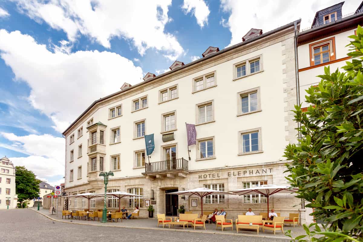 Das Hotel Elephant in Weimar in klassischer Architektur, mit Sonnenschirmen und Sitzgelegenheiten.