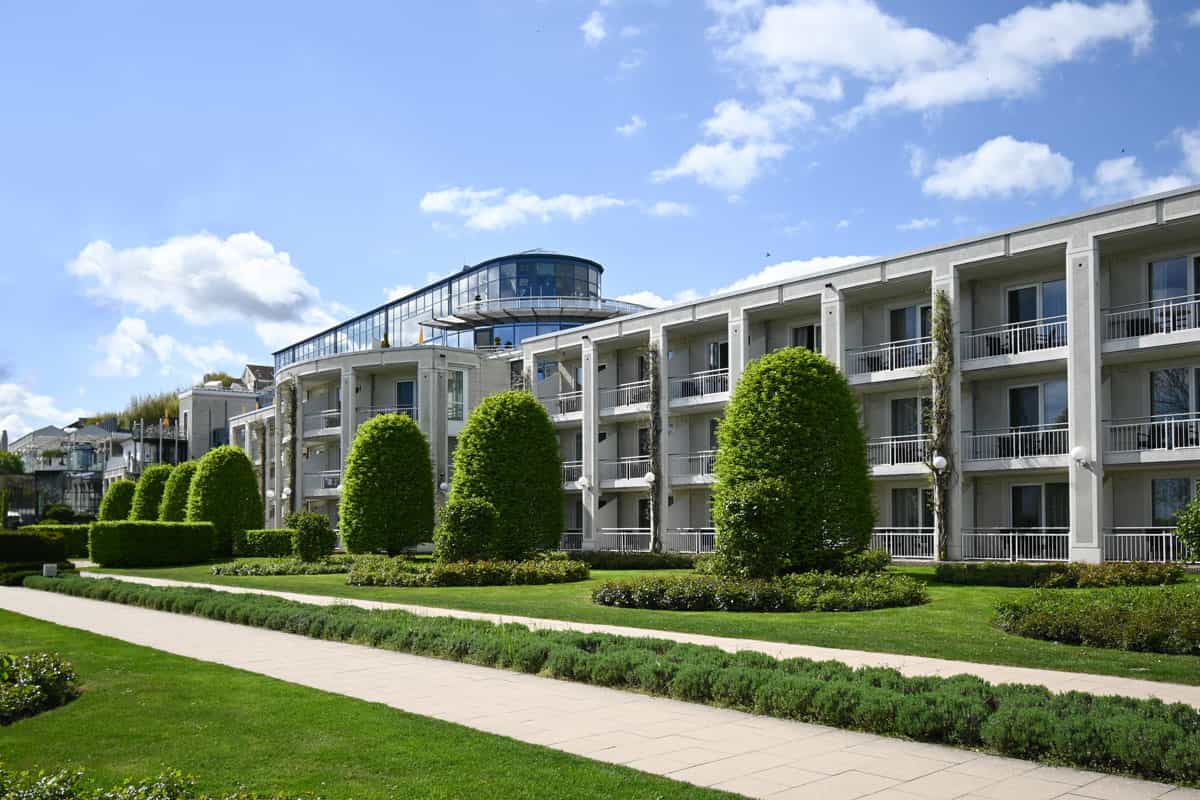Außenansicht des Hotel Kaiserhof in Heringsdorf mit Balkonen, gepflegten Grünflächen und einem gläsernen Aufbau.