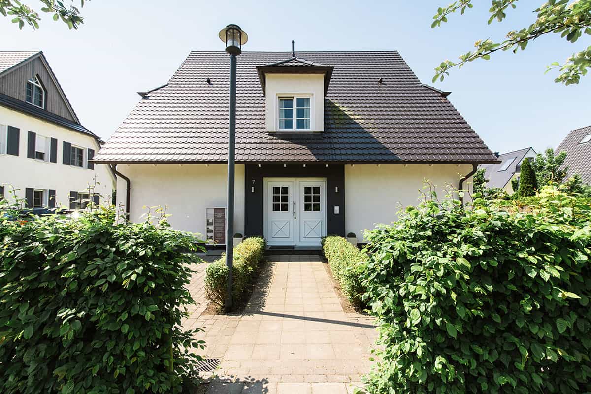 Haus der Residenz Seezeichen in Ahrenshoop mit dunklem Dach, Hecken und gepflastertem Weg.