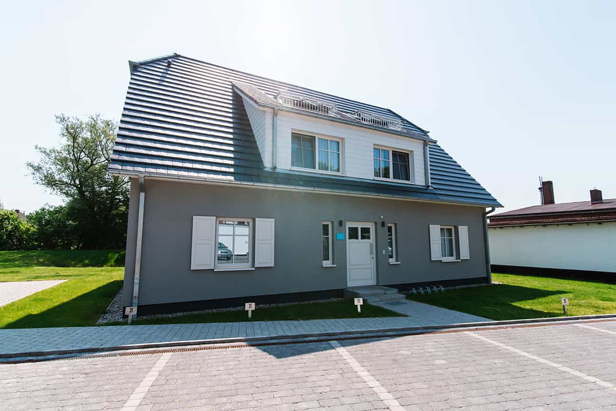 Strandvilla Seezeichen in Ahrenshoop mit weißen Fensterläden, großem Dach und gepflegtem Garten.