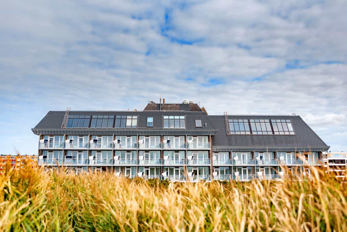 Außenansicht des Wyn Strandhotels auf Sylt, umgeben von Gräsern unter leicht bedecktem Himmel.