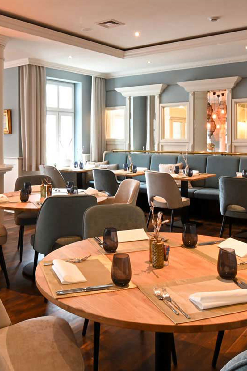 Blick in das maritime Restaurant Küstensilber mit hellen Stühlen und Bänlen, Holzdekor und eingedeckten Tischen im Vju Hotel auf Rügen.