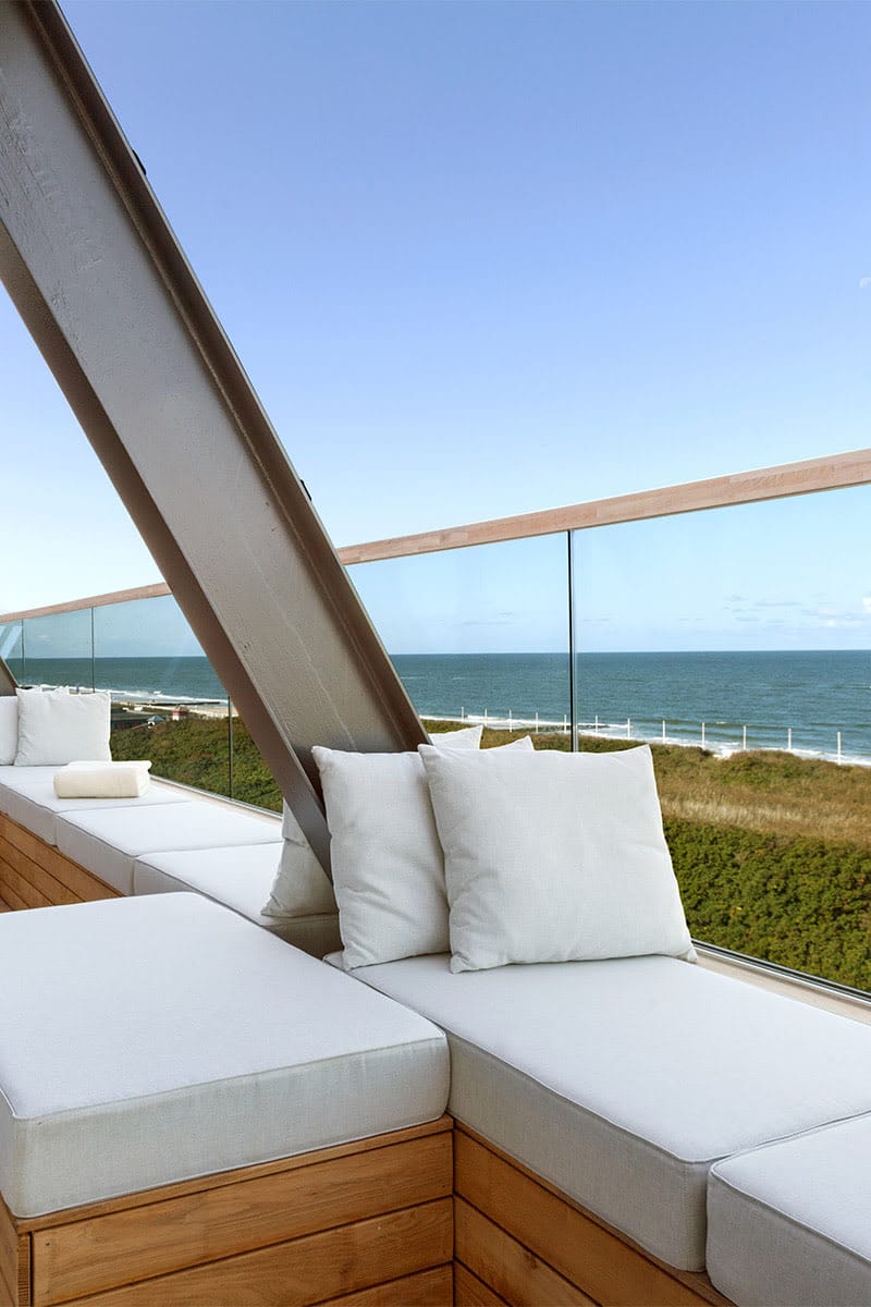 Moderne Terrasse des Wyn Strandhotels Sylt mit weißen Sitzpolstern und Blick auf das Meer und Dünen.