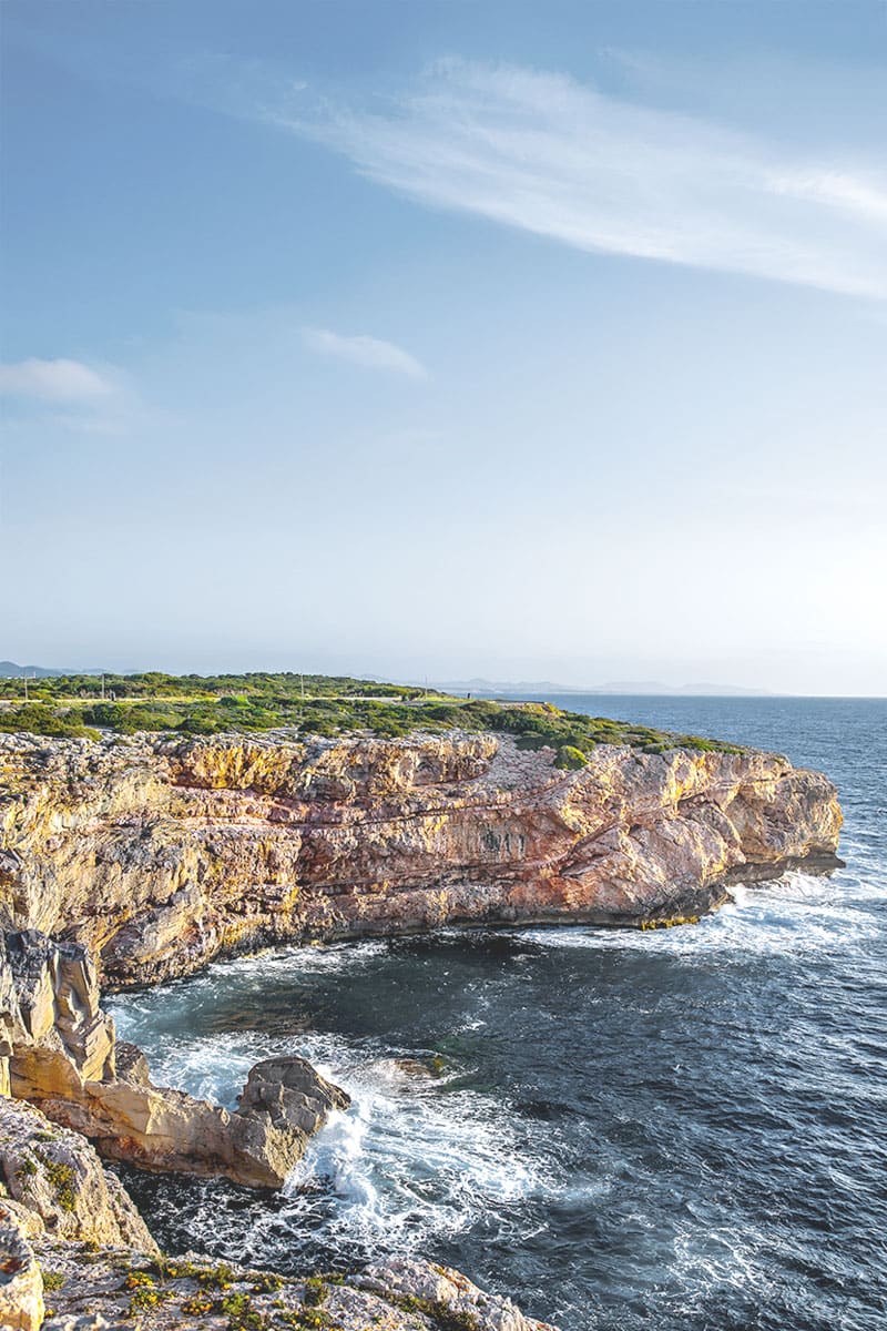 Küstenlandschaft auf Mallorca mit steilen Felsen und ruhigem Meer, umgeben von üppiger Natur.