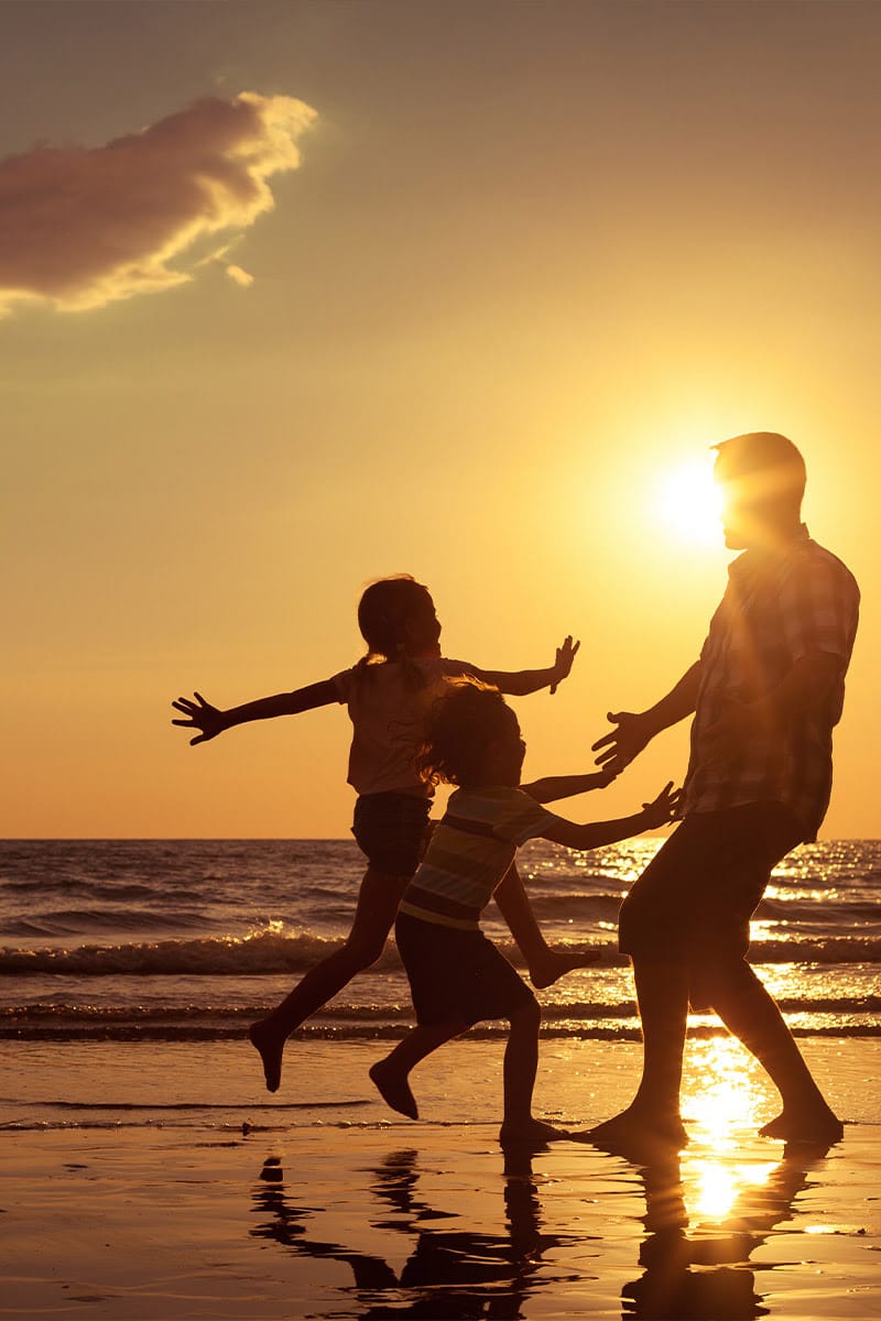 Family playing on the beach in the sunset, two children running towards their father.