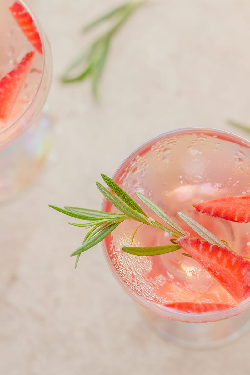 Glass with sparkling summer drink, decorated with fresh strawberries and rosemary, refreshing look.
