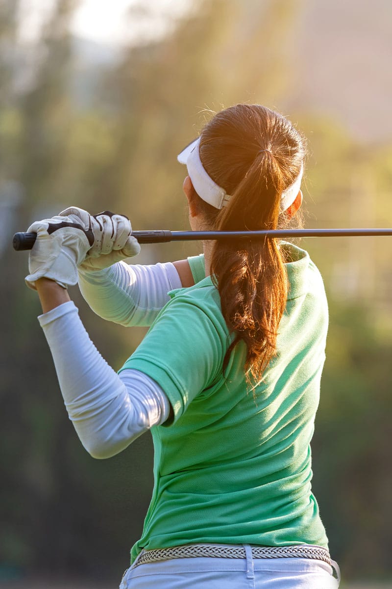 Frau beim Golfschwung auf einem grünen Golfplatz, konzentrierte Haltung und sonnige Umgebung.
