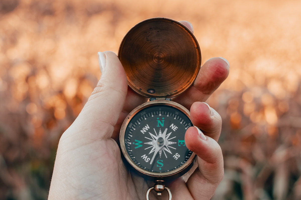 Nahaufnahme einer Hand, die einen Kompass draußen in der Natur hält.