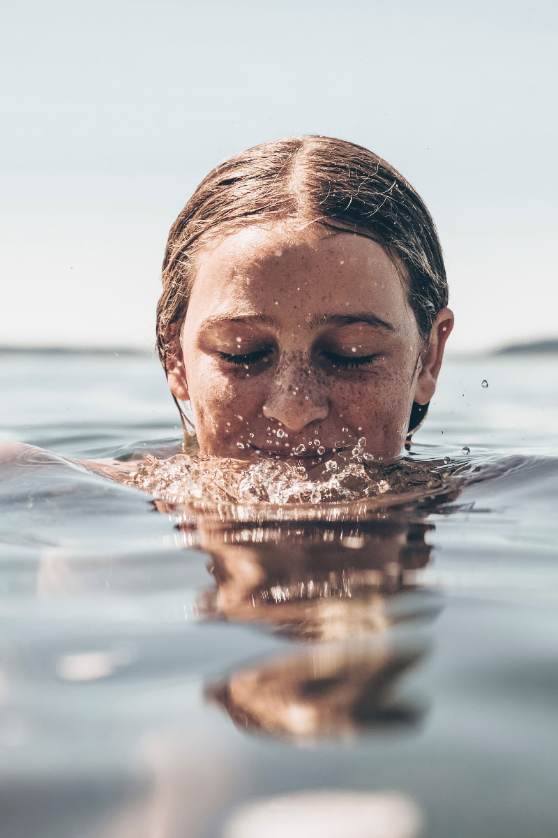 Nahaufnahme einer Person, die mit geschlossenen Augen im Wasser schwimmt und das Gesicht leicht eintaucht.