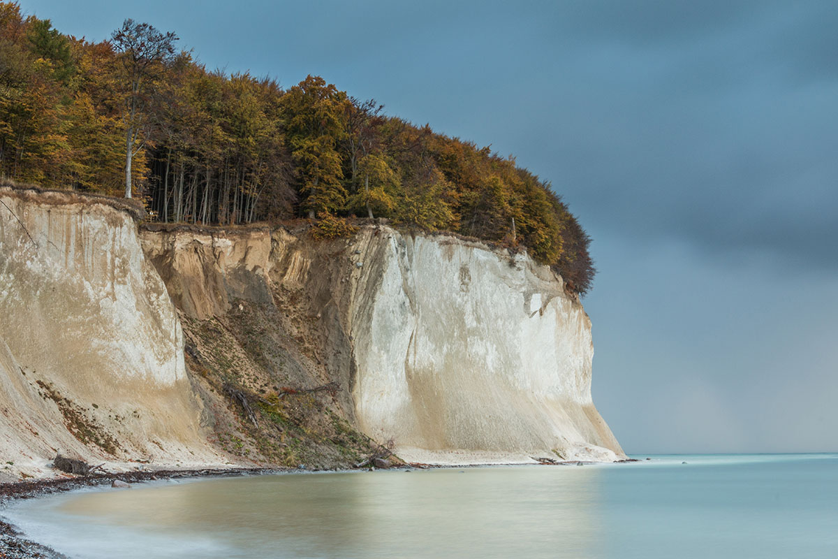 Hohe weiße Kreidefelsen auf Rügen mit Herbstbäumen auf der Spitze, die sich über das ruhige Meer erheben.