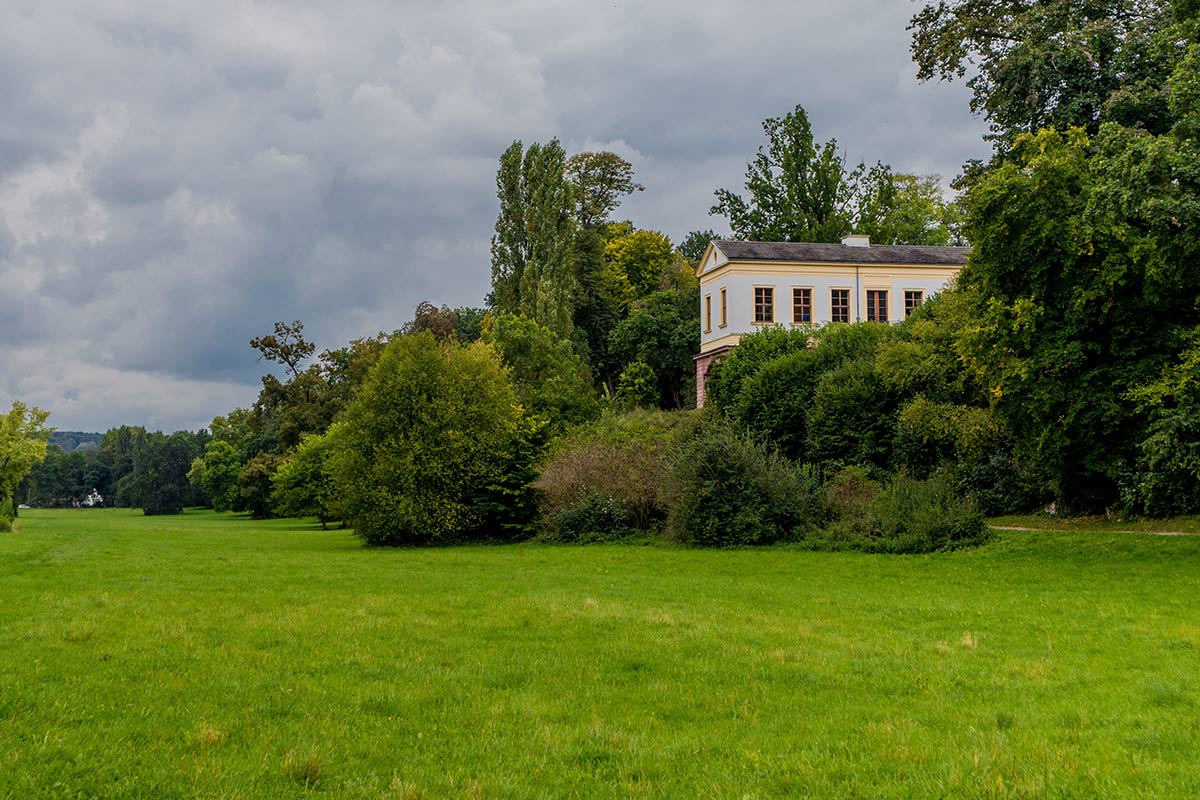 Ein altes Herrenhaus auf einer weiten, grünen Wiese, umgeben von dichten Bäumen.