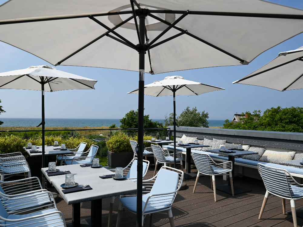 Moderne Terrasse mit weißen Sonnenschirmen, gepolsterten Sitzgelegenheiten und direktem Blick auf das Meer.