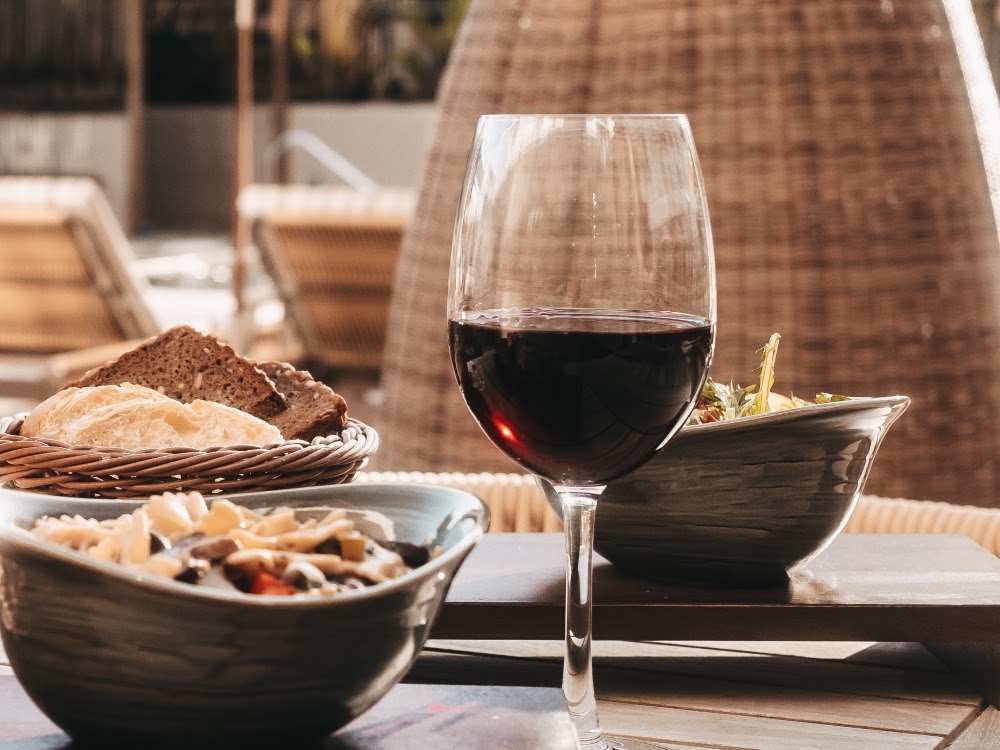 Ein gedeckter Tisch mit einem Glas Rotwein, Schalen mit Speisen und einem Korb Brot im Außenbereich.