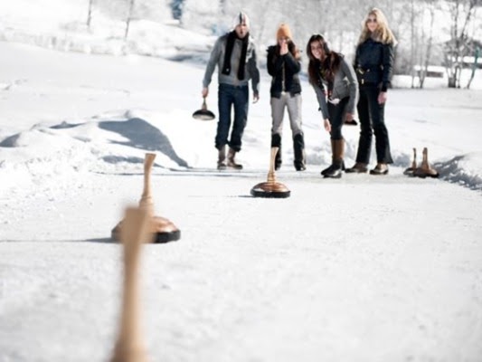 Gruppe von vier Personen beim Eisstockschießen auf einer verschneiten Bahn in einer Winterlandschaft.