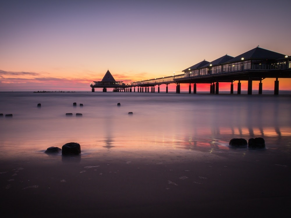 Die Seebrücke Heringsdorf auf Usedom bei Sonnenuntergang, das ruhige Meer im Vordergrund.