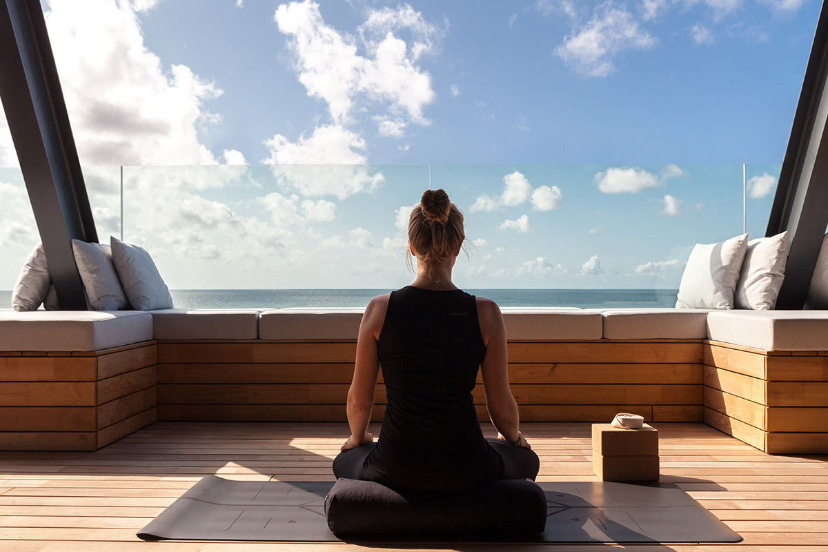 Woman meditating on a wooden terrace with a sea view in sunny weather and clear sky.